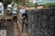 A woman leaning against a stone wall in a park.