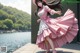 A woman in a pink dress and hat is dancing by the water.