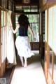 A woman in a blue top and white skirt walking down a hallway.